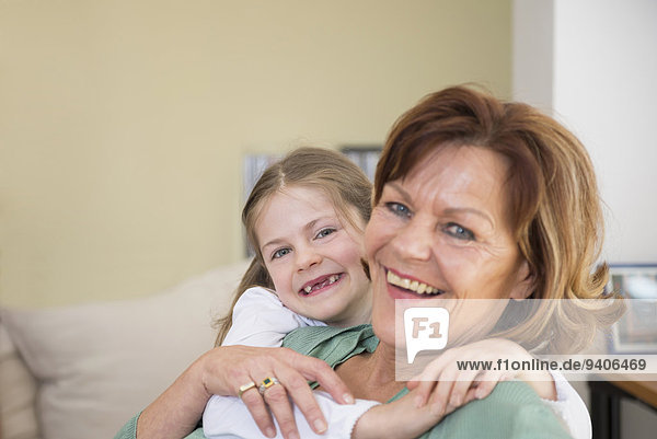 Portrait of grandmother and granddaughter sitting on couch in living room  smiling