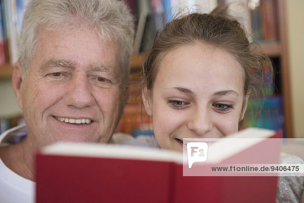 Grandfather and granddaughter reading book on couch in living room  smiling