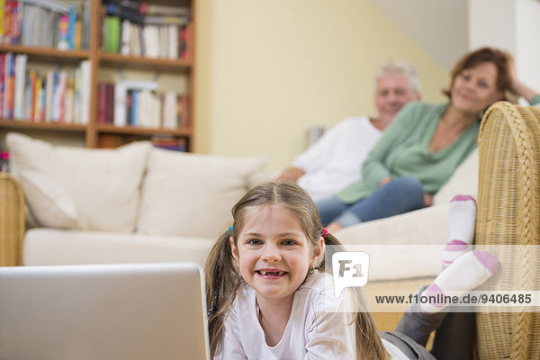 Granddaughter using laptop in living room while grandparents in background