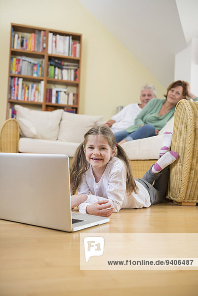 Granddaughter using laptop in living room while grandparents in background