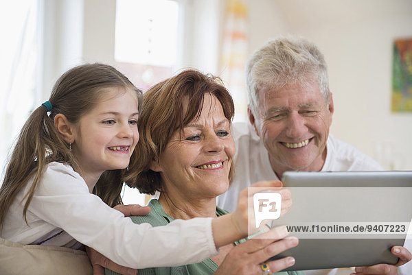 Grandparents and granddaughter looking in digital tablet  smiling