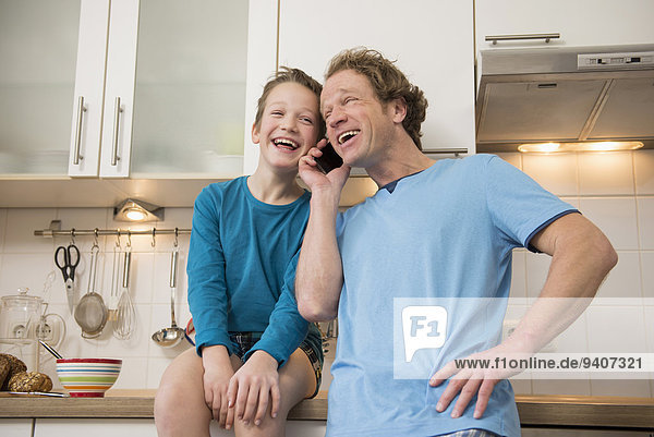Laughing father and son with cell phone in kitchen
