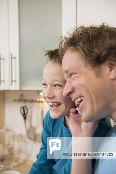 Laughing father and son with cell phone in kitchen