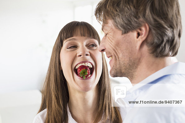 Mid adult woman carrying strawberry in mouth while man smiling  close up