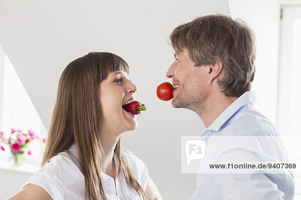 Couple carrying strawberry and tomato in mouth