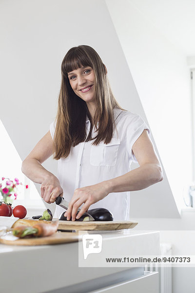 Portrait of mid adult woman cutting aubergine in kitchen  smiling