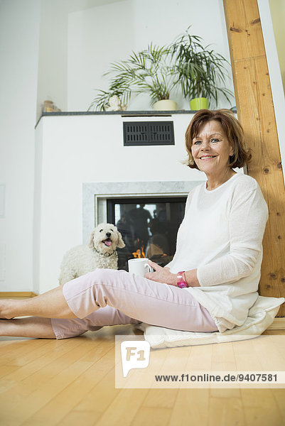Portrait of senior woman with dog sitting in front of fireplace  smiling