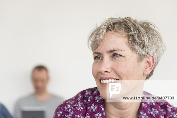 Portrait of mature smiling woman while mature man using digital tablet in the background