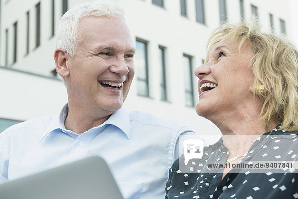 couple sitting on a bench  holding tablet computer and laughing