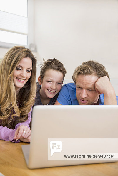 Happy family lying on floor looking at laptop