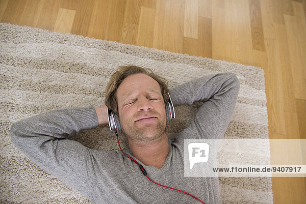 Relaxed man lying on rug listening to music