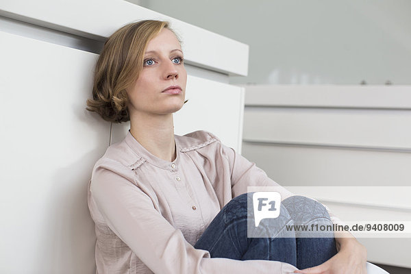 Serious young woman leaning against chest of drawers