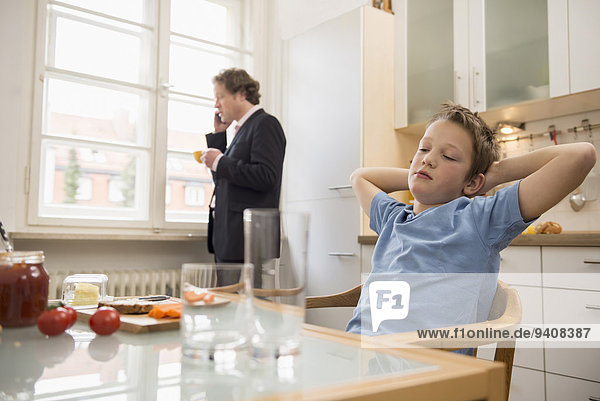 Bored boy in kitchen with father on the phone in background
