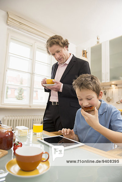 Boy using digital tablet during breakfast with father watching