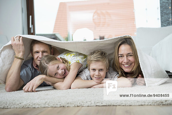 Happy family with two kids at home  lying on floor under blanket