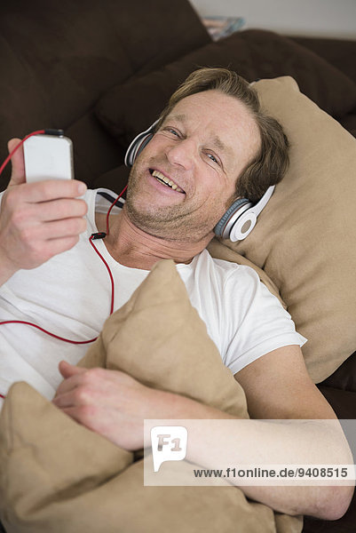 Man lying on couch with headphones and smartphone