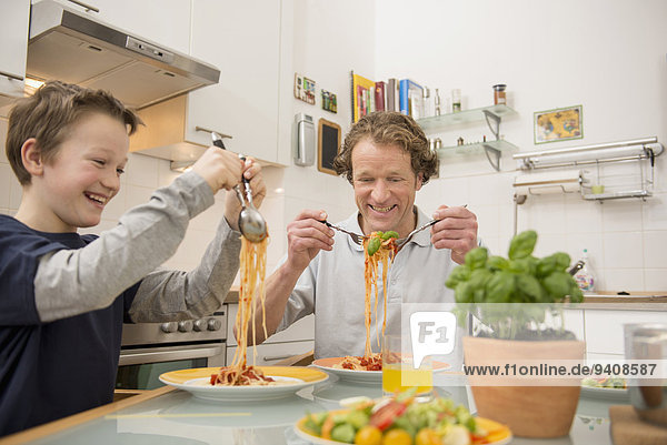 Father and son eating spaghetti and salad in kitchen