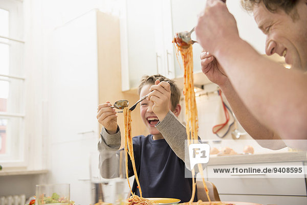 Father and son eating spaghetti in kitchen