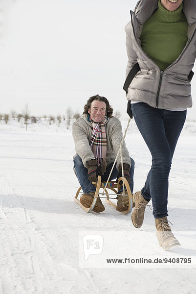 Woman dragging man on sledge in snow