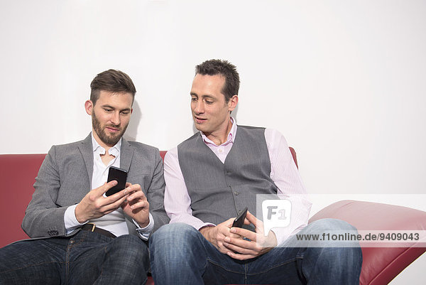 Two young men sitting office sofa mobile phone