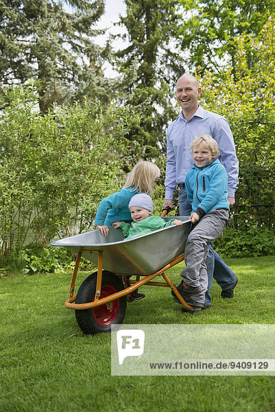 Father in garden pushing kids in wheelbarrow