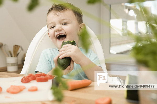 Boy eating cucumber in kitchen  smiling
