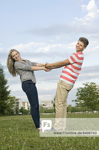 Portrait of teenage couple holding hands in park  smiling
