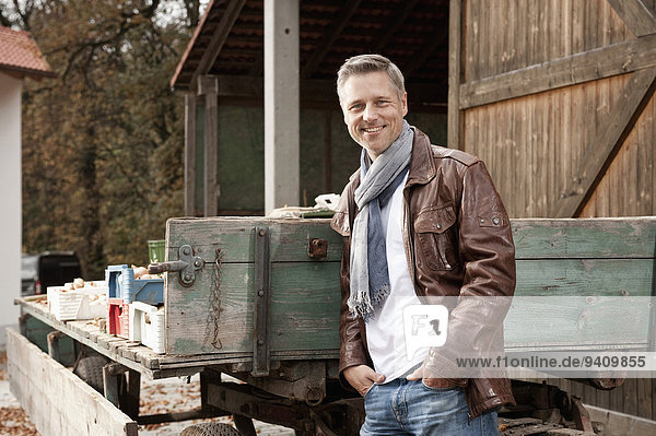 Smiling man leaning against trailer on farm