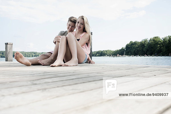 Teenage couple sitting on a jetty at lake