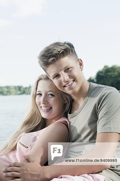 Portrait of teenage couple sitting on a jetty at lake
