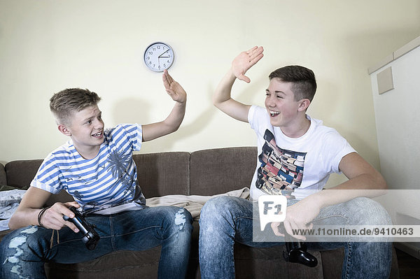 Two teenage boys with video game controllers high fiving