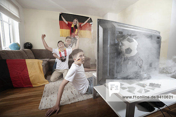 Teenage soccer fans in living room with ball demolishing TV
