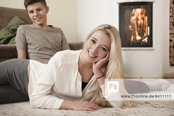 Teenage couple relaxing on carpet in front of fireside