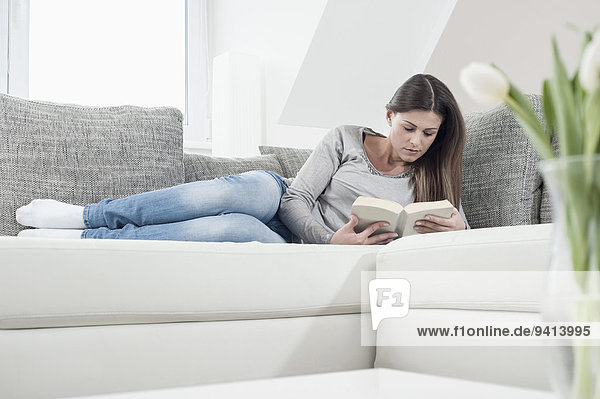 Young woman reading a book on her couch at home