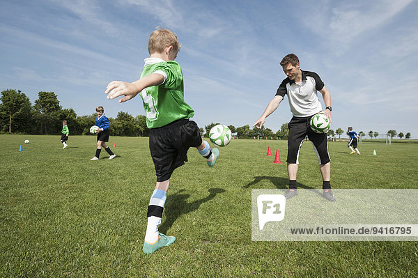 Soccer trainer teaching young player helping