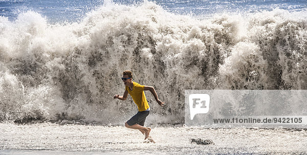 Junger Mann mit Sonnenbrille rennt vor einer hohen Welle weg,  La Palma,  Kanarische Inseln,  Spanien