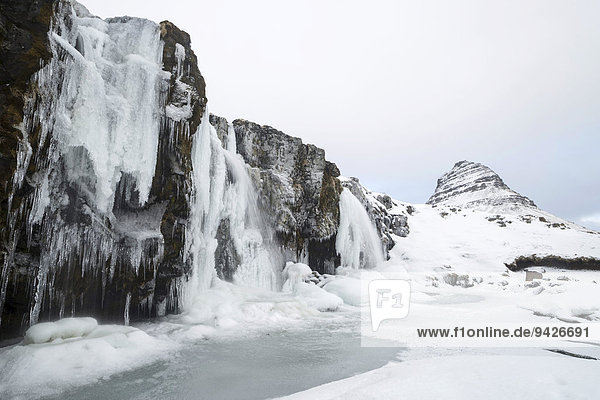 Berg Kirkjufell hinter gefrorenem Wasserfall Kirkjufellsfoss im Schnee Snaefellsnes Halbinsel Island