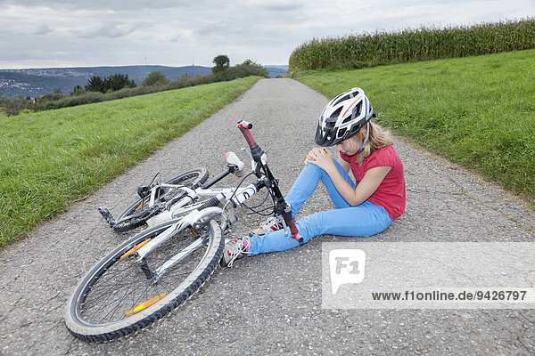 Girl  9 years  wearing a bicycle helmet  holding her knee after crashing with her bicycle