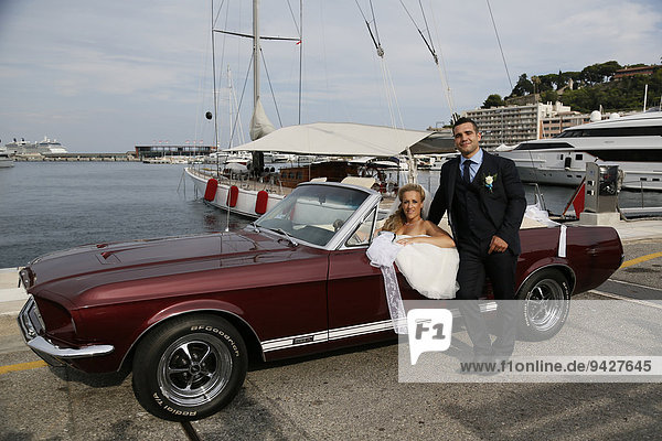 Braut und Bräutigam posieren mit einem offenem Ford Mustang am Hafen