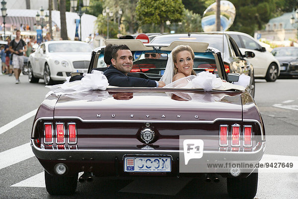 Bride and groom riding in an open Ford Mustang convertible car through the city  Monaco
