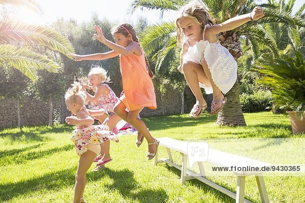 Five energetic girls jumping from garden bench