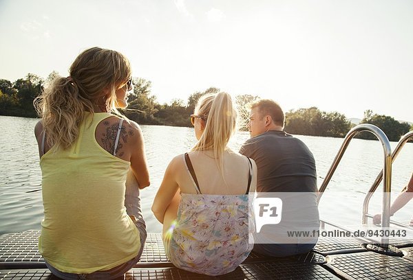 Drei junge erwachsene Freunde  die vom Pier am Flussufer blicken
