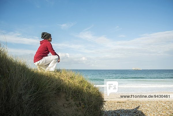 Reife Frau kauernd und mit Blick aufs Meer  Camaret-sur-mer  Bretagne  Frankreich
