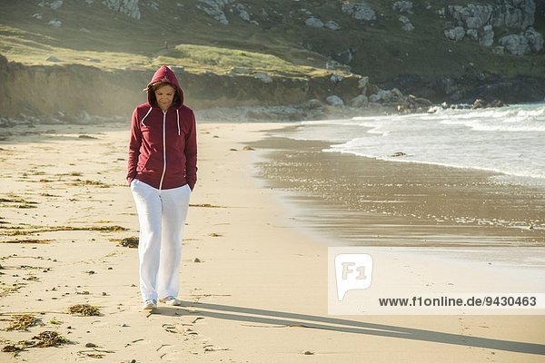 Reife Frau beim Strandspaziergang mit den Händen in den Taschen  Camaret-sur-mer  Bretagne  Frankreich