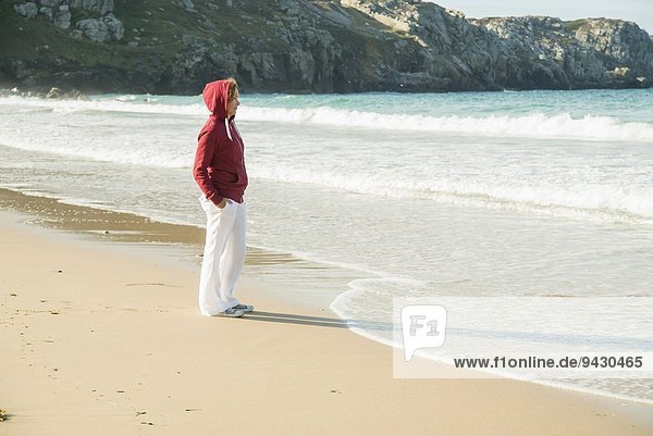 Reife Frau am Strand stehend mit Händen in den Taschen  Camaret-sur-mer  Bretagne  Frankreich