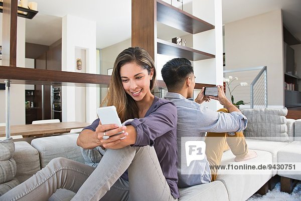 Rücken an Rücken Pärchen beim Spielen auf Smartphones auf dem Wohnzimmersofa