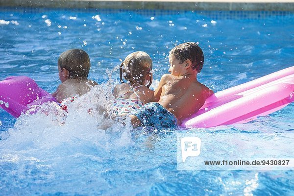 Rear view of three children playing on inflatable mattress in garden swimming pool