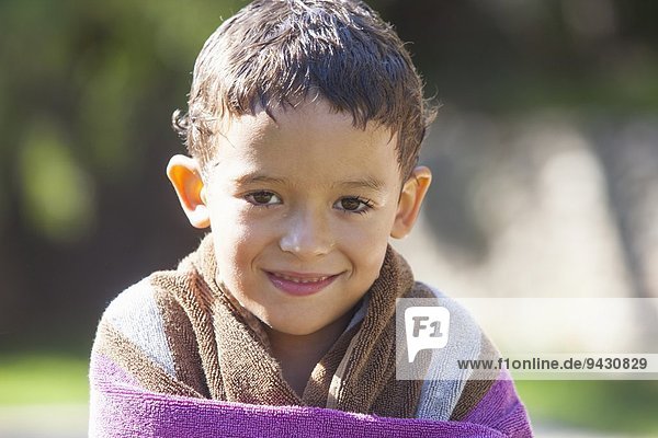 Porträt eines Jungen mit nassen Haaren in Handtuch gewickelt im Garten