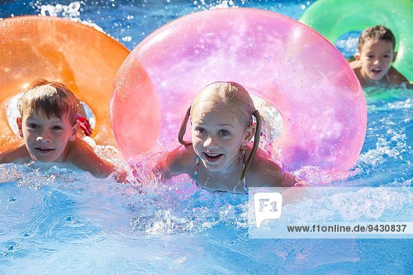 Drei Kinder schwimmen mit aufblasbaren Ringen im Gartenschwimmbad