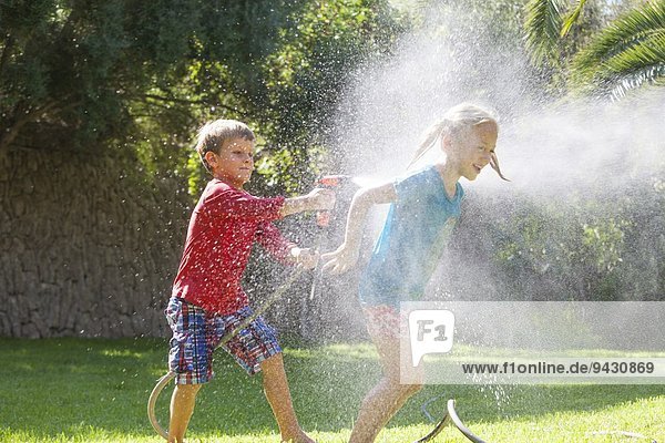 Junge spritzendes Mädchen im Garten mit Wasserberieselung